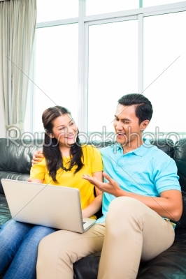 Asian couple using laptop on sofa