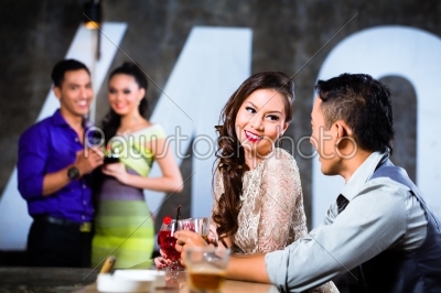 Asian couples flirting and drinking at nightclub bar 