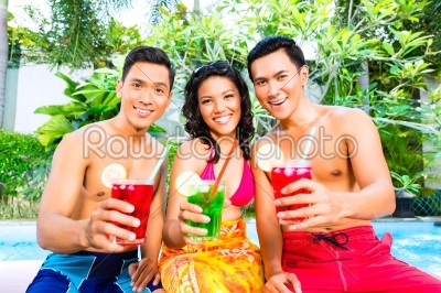 Asian friends drinking cocktails at pool