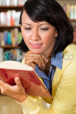 Asian girl in library reading a book