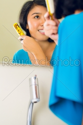 Asian woman combing hair in bathroom mirror