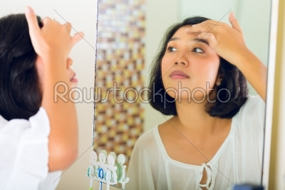 Asian woman discovering a pimple in face