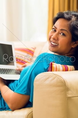 Asian Woman sitting on couch surfing the internet and smiling