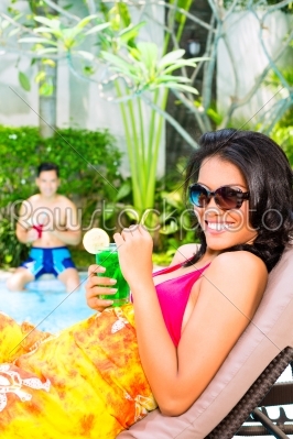 Asian woman tanning at pool with cocktail