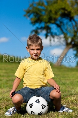 Boy with football sitting on a meadow