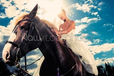 Bride in wedding dress riding a horse, backlit