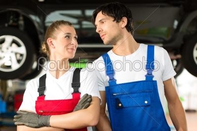 Car mechanics male and female in front of auto