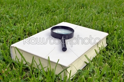 Closed book with magnifying glass and green background