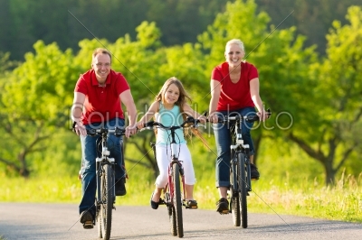 Family with kid cycling in summer with bicycles