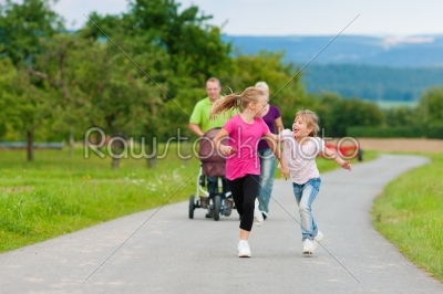 Family with three children (one baby lying in a baby buggy) walking down a path outdoors, the two older daughters running ahead