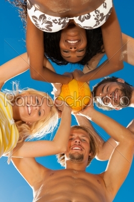 Group of friends - women and men - playing beach volleyball, conceptional shot with all of them looking down with the ball at the camera