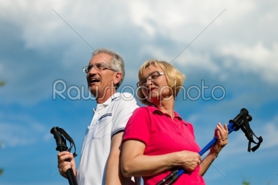 Happy mature or senior couple doing Nordic walking in summer