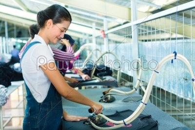 Indonesian worker with flat iron in textile factory
