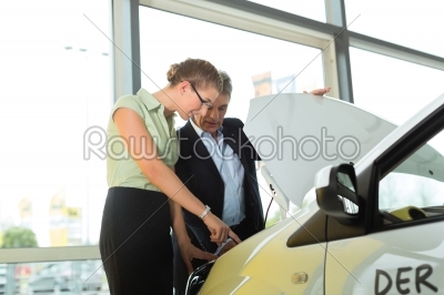 man and woman in car dealership looking under  a hood