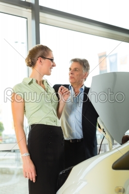 man and woman in car dealership looking under  a hood