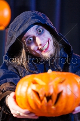 Man in scary Halloween costume holding pumpkin