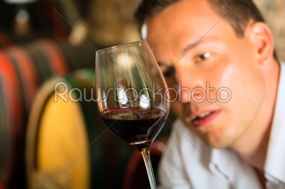 Man testing wine in background barrels