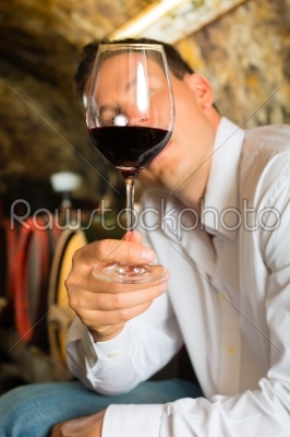Man testing wine in background barrels