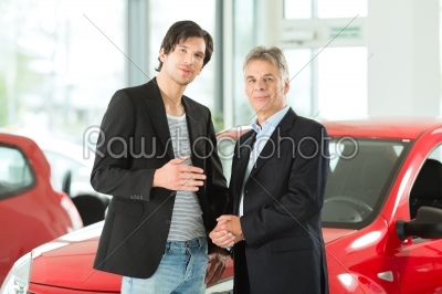 Mature and young man with autos in car dealership