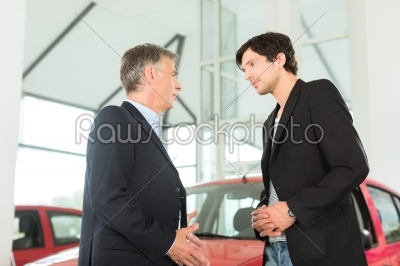 Mature dealer and young man with auto in car dealership