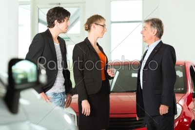 Mature man with young couple and autos in car dealership
