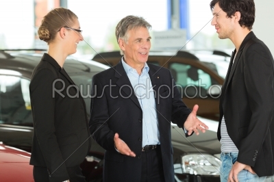 Mature man with young couple and autos in car dealership