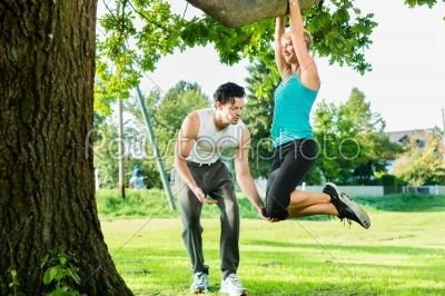 People in city park doing chins or pull ups on tree
