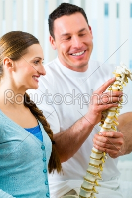 Physiotherapist in his practice, he explains a female patient the vertebral column and the emergence of back pain