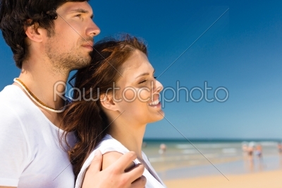 Playful couple on the ocean beach enjoying their summer vacation, he embraces her