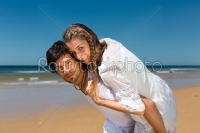 Playful couple on the ocean beach enjoying their summer vacation, the man is carrying the woman piggyback