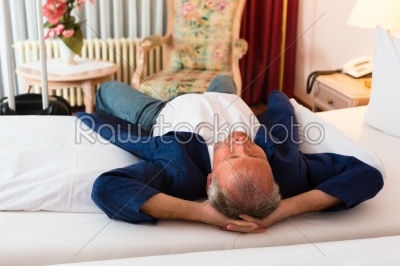 Senior man lying on the bed in the hotel room