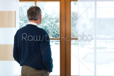 Senior man standing at the window looking out