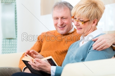 Seniors at home reading a book together 