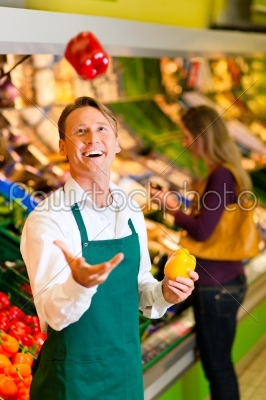 Shop assistant in a supermarket at the vegetable shelf; he is tossing a bell pepper