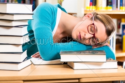 student in library asleep over books