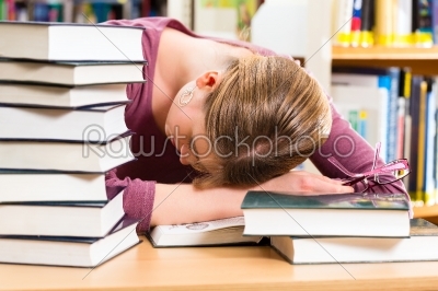 student in library asleep over books