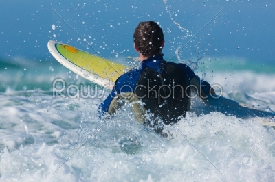 Surfer with his board in the waves entering the sea, FOCUS is on the wave crashing on man!