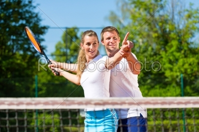 Tennis teacher helping woman to play