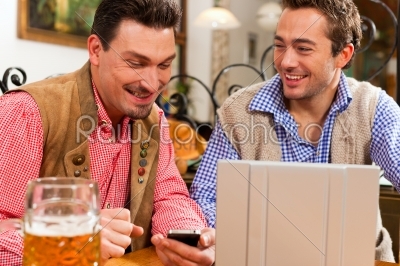 Two friends in Bavarian pub with laptop