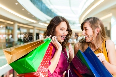Two girls shopping in mall looking in bags