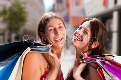 Two women being friends shopping downtown with colorful shopping bags, they are walking down a street having fun