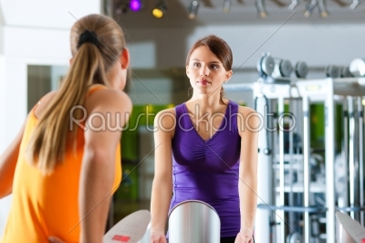 Two women in gym in front of a exercising machine