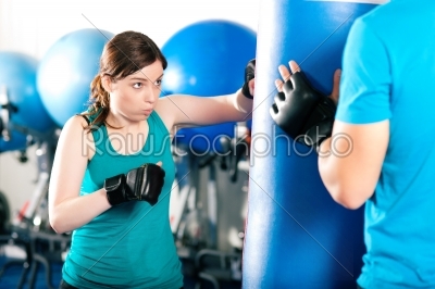 Woman Boxer hitting the sandbag, her trainer is assisting