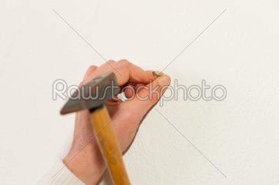Woman is driving a nail into a wall