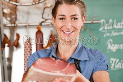 Woman or female butcher with raw ham in butchers shop