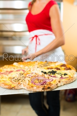 Woman pushing the finished pizza from the oven