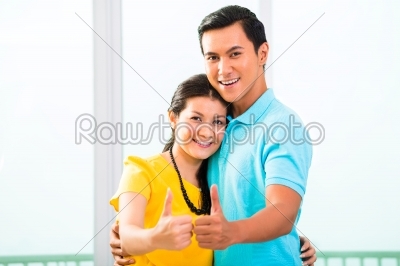 Young Asian couple in apartment with thumbs up