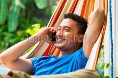 Young asian man in hammock with phone