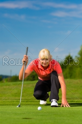 Young female golf player on course aiming for put