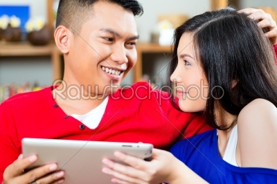 Young Indonesian couple - man and woman - sitting with a tablet computer on a couch